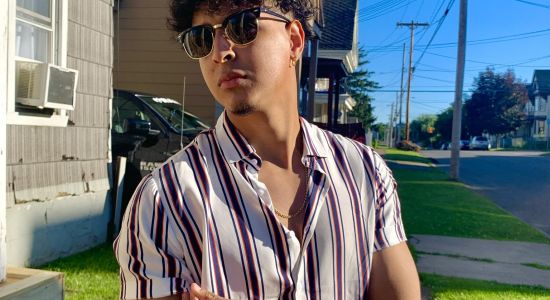 A photo of Enmanuel Outside wearing sunglasses looking away and wearing a short sleeve striped button down shirt