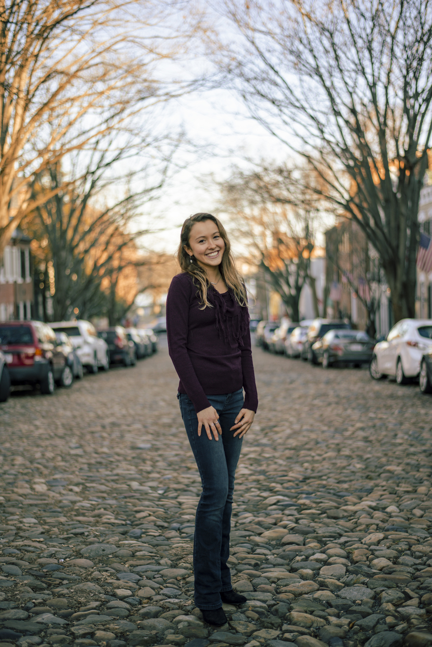 Photo of Kaycie on cobblestone road in a purple sweater and dark blue jeans