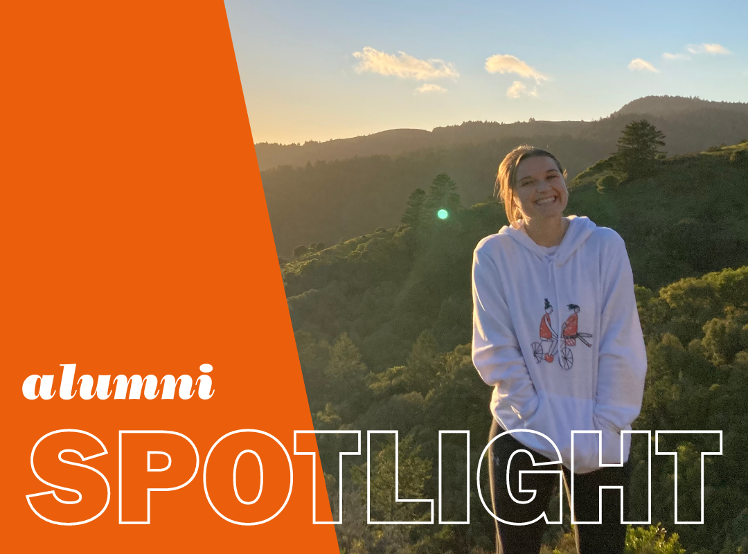 Photo of Claire in a hoodie with hands in pocket standing against hilly background. Has overlay that reads, "alumni spotlight". 