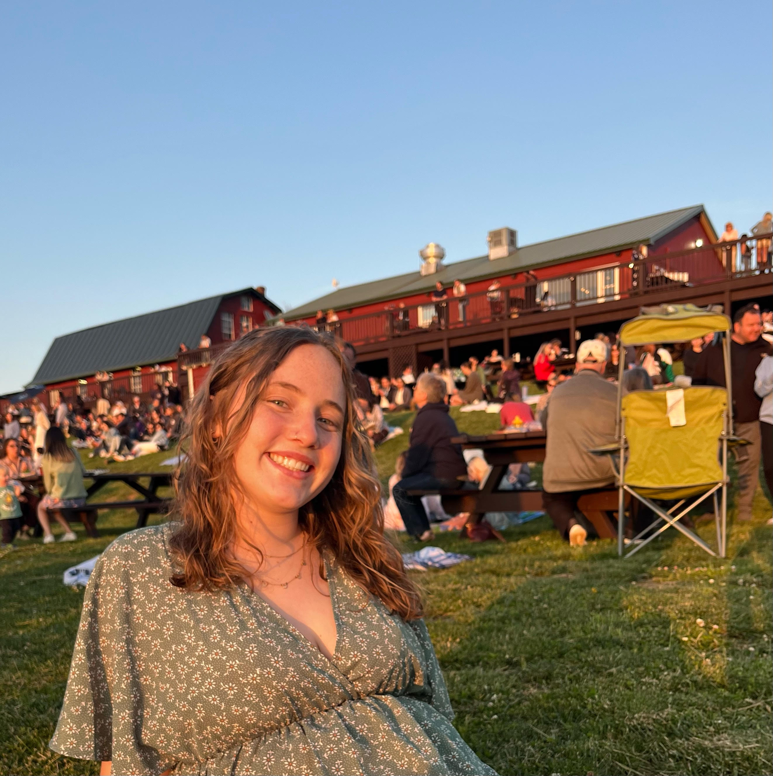 Photo of Bibby outside at Carter's Mountain, sitting on a hill with people picnicking in the background. 