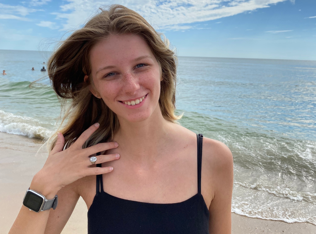 Photo of Jordan on the beach smiling at camera with one hand in hair