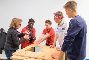 Student Chris Sausa, right, and his “little brother” Johan, center, along with student Garrett Lukens, build doghouses with Sharon Shafer from Houses of Wood and Straw, left, and NBC-29 reporter Moriah Davis. (Photos by Peggy Harrison)